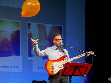 Gitarrist wirft einen orangefarbenen Luftballon während einer Aufführung.